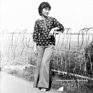 Woman stands near barbed wire fence in a black and white photo.