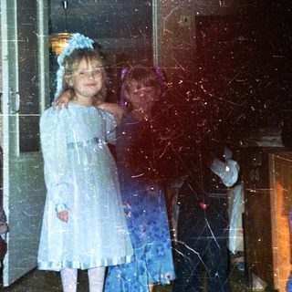 Two young girls in dresses stand near a bedroom.