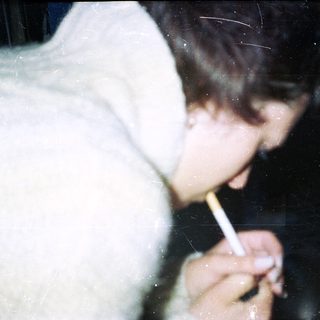 Person holding a lit cigarette in a dimly lit setting.