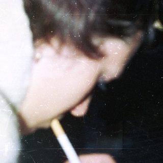 Person holding a lit cigarette in a dimly lit setting.