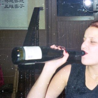 Woman struggles to open a wine bottle, smoking a cigarette.