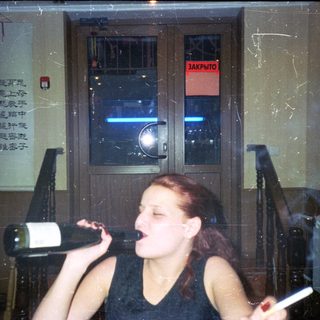 Woman struggles to open a wine bottle, smoking a cigarette.