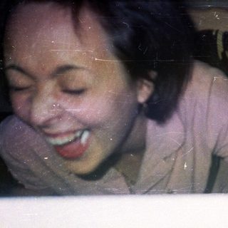 Here's a brief summary of the image: Person smiling, reaching over a table with a pink shirt.