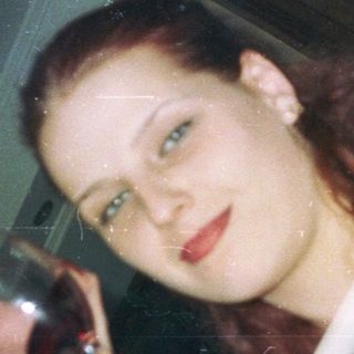 Woman holds wine glass, looking directly at the camera.