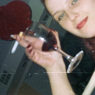 Woman holds wine glass, looking directly at the camera.