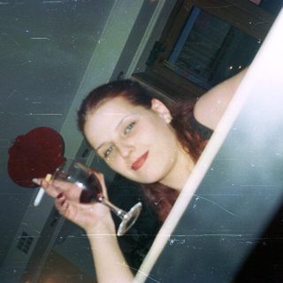 Woman holds wine glass, looking directly at the camera.