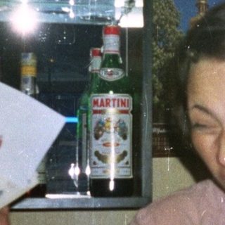 Woman smiles, holding paper in front of a bar.
