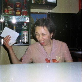 Woman smiles, holding paper in front of a bar.