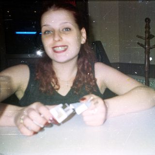 Here's a brief summary of the image: Woman holding a small object, smiling in a dimly lit room.