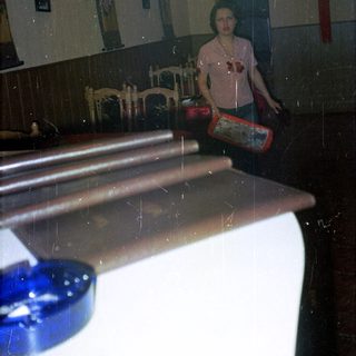 Person stands near tables in a dimly lit restaurant.