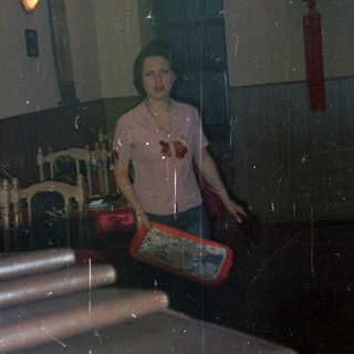 Person stands near tables in a dimly lit restaurant.
