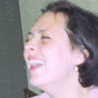 A smiling woman sits at a table in a restaurant.