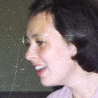Woman seated at a table, holding a piece of paper.