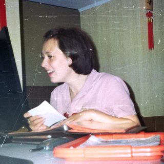 Woman seated at a table, holding a piece of paper.