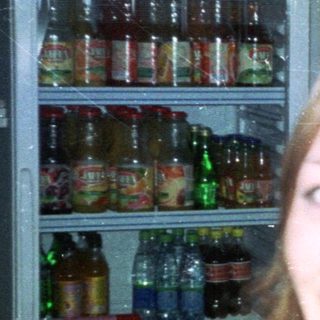 Woman sits in a bar, smiling near a refrigerator.