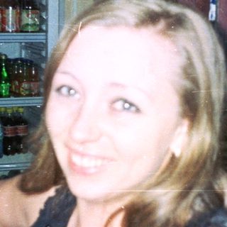 Woman sits in a bar, smiling near a refrigerator.