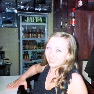 Woman sits in a bar, smiling near a refrigerator.