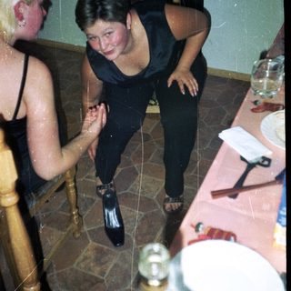 Woman in black dress playfully poses near table setting.