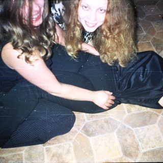 Woman sitting, another lying down, both smiling on tiled floor.