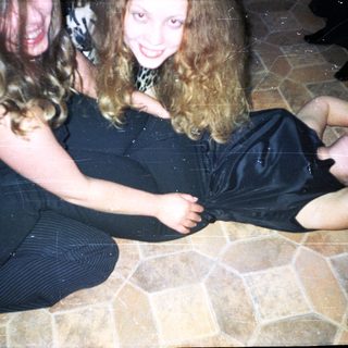 Woman sitting, another lying down, both smiling on tiled floor.