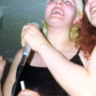 Two women holding a microphone, laughing and looking up.