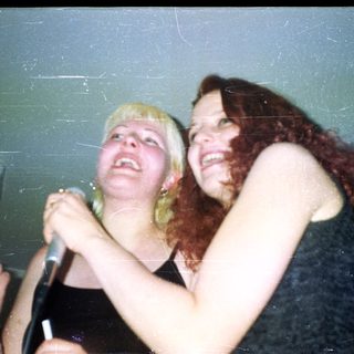 Two women holding a microphone, laughing and looking up.