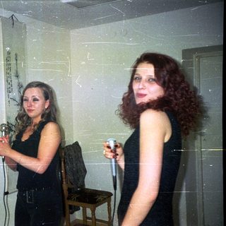 Two women holding microphones in a sparsely decorated room.