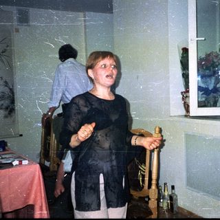 Woman holds a bottle, standing in a decorated room.