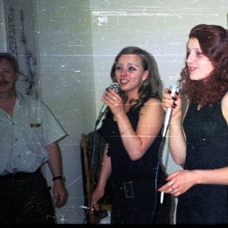 Two women sing into microphones at an indoor gathering.
