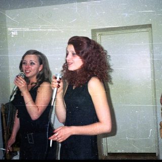 Two women sing into microphones at an indoor gathering.