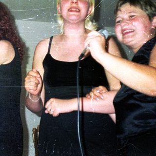 Three women holding microphones, singing or performing onstage.