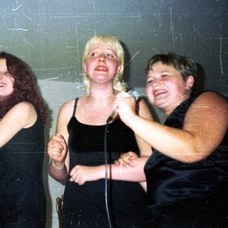 Three women holding microphones, singing or performing onstage.