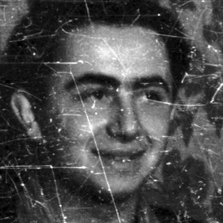 Black and white portrait of a man indoors with patterned wallpaper.