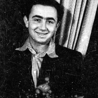 Here's a brief summary of the image: Black and white portrait of a smiling man in a suit.