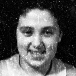 Here's a brief summary of the image: Woman in vintage dress smiles for a black and white portrait.