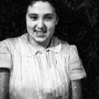 Here's a brief summary of the image: Woman in vintage dress smiles for a black and white portrait.