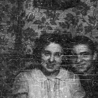 Here's a brief summary of the image: Two men appear in a faded, scratched black and white photograph.