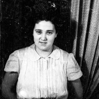 Here's a brief summary of the image: Black and white portrait of a woman with a patterned curtain background.
