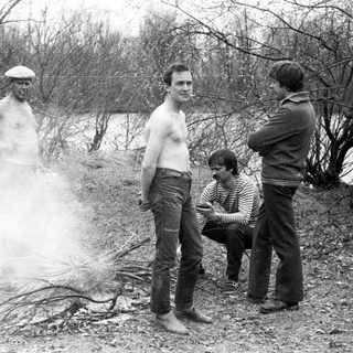Men standing and sitting near a smoky fire outdoors.