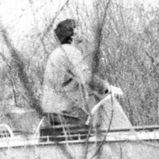 Man in boat along riverbank, obscured by branches.
