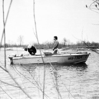 Men in a boat travel along a riverbank.