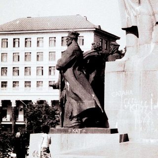 Monumen with graffiti, soldiers stand nearby in a public space.