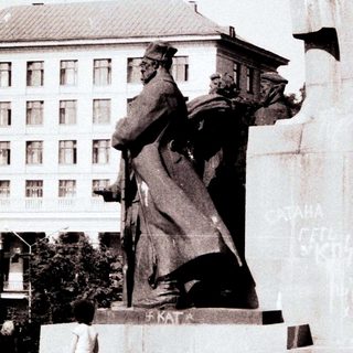 Monumen with graffiti, soldiers stand nearby in a public space.