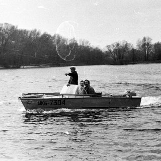Two men in a boat travel across a body of water.