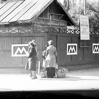 Two women stand near a fence with a sign.