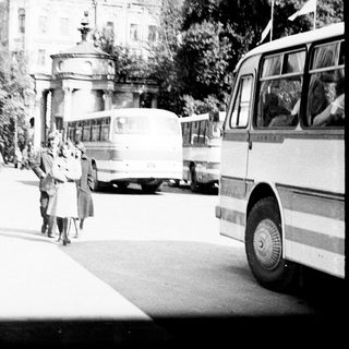 People walking near buses in a vintage, black and white scene.
