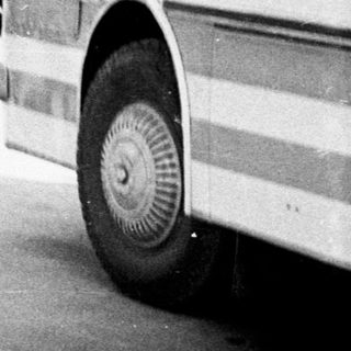 People walking near buses in a vintage, black and white scene.
