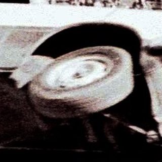 Man stands atop an overturned car in a stadium.