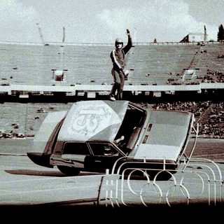 Man stands on a car in a stadium.