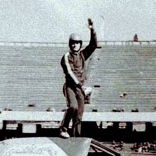 Man stands on a car in a stadium.